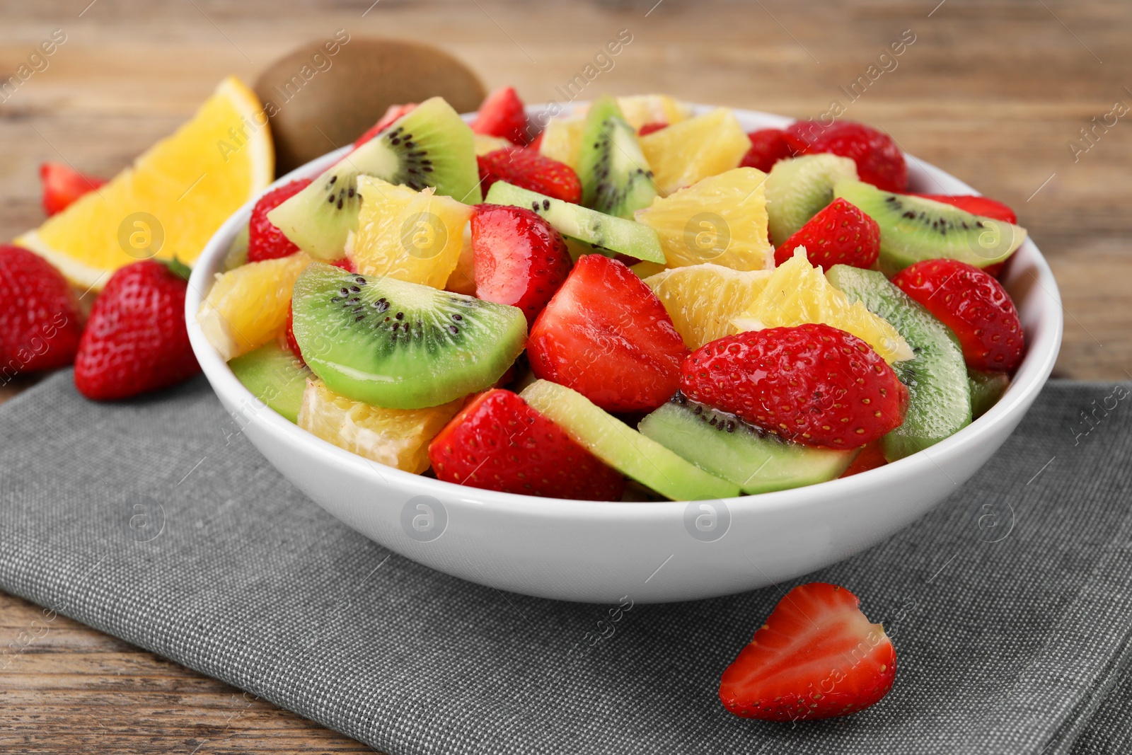 Photo of Delicious fresh fruit salad in bowl on wooden table, closeup