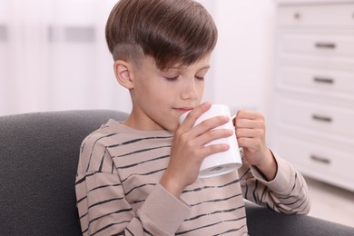 Cute boy drinking from white ceramic mug on sofa at home