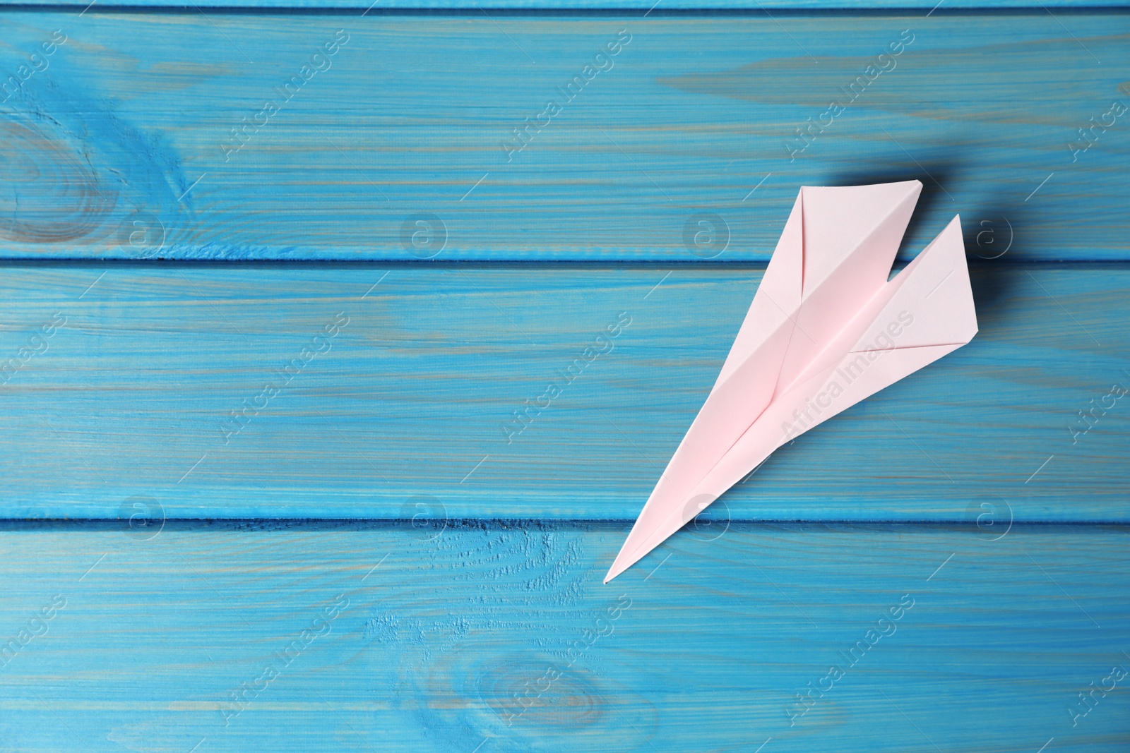 Photo of Handmade paper plane on light blue wooden table, top view. Space for text