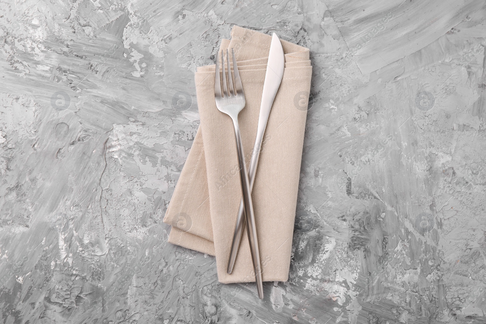 Photo of Elegant silver cutlery and kitchen towel on grey textured table, top view
