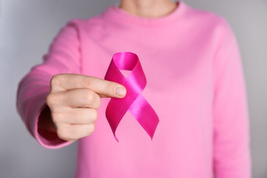 Woman holding pink ribbon on grey background, closeup. Breast cancer awareness