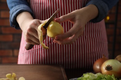 Photo of Woman peeling fresh potato with knife at table indoors, closeup