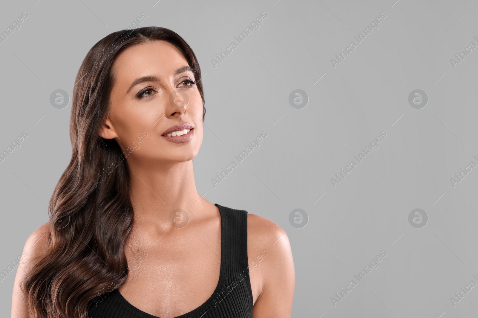 Photo of Hair styling. Beautiful woman with wavy long hair on grey background, space for text