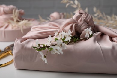 Photo of Furoshiki technique. Gift packed in pink fabric and beautiful flowers on white table, closeup
