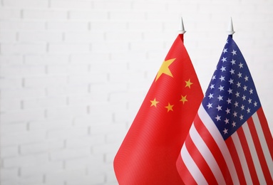 USA and China flags against white brick wall, space for text. International relations