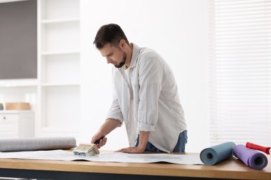 Photo of Man applying glue onto wallpaper sheet at wooden table indoors