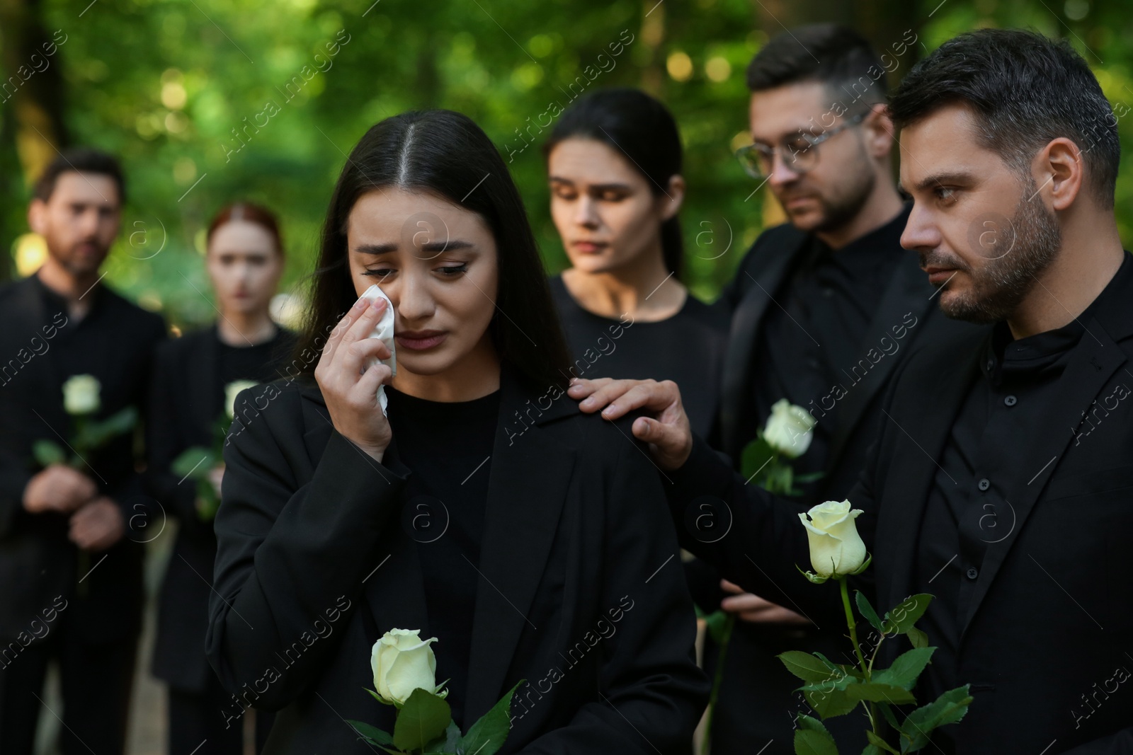 Photo of Funeral ceremony. Sad people with white rose flowers mourning outdoors