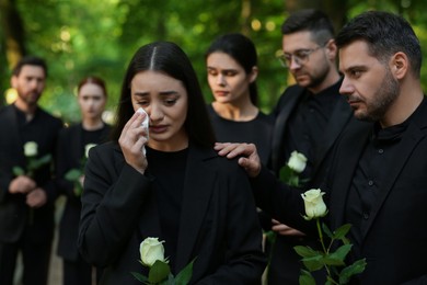 Funeral ceremony. Sad people with white rose flowers mourning outdoors