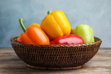 Photo of Wicker bowl with ripe bell peppers on wooden table against light blue background