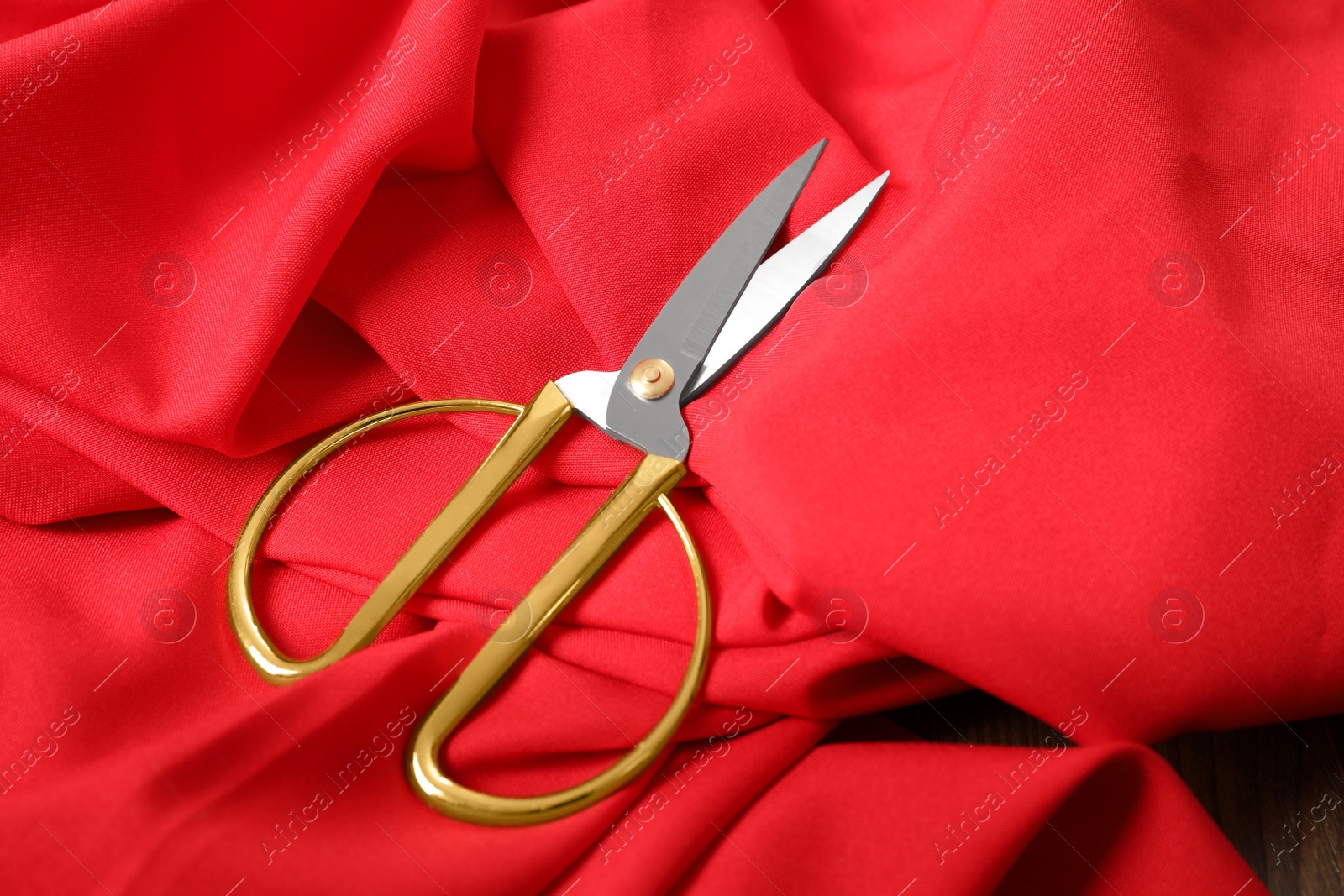 Photo of Red fabric and sharp scissors on wooden table. Space for text