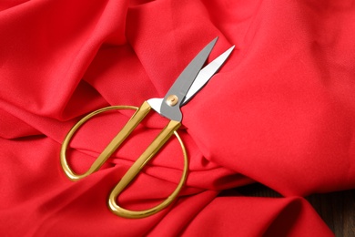 Photo of Red fabric and sharp scissors on wooden table. Space for text