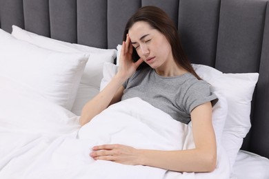 Sad woman suffering from headache in bed indoors