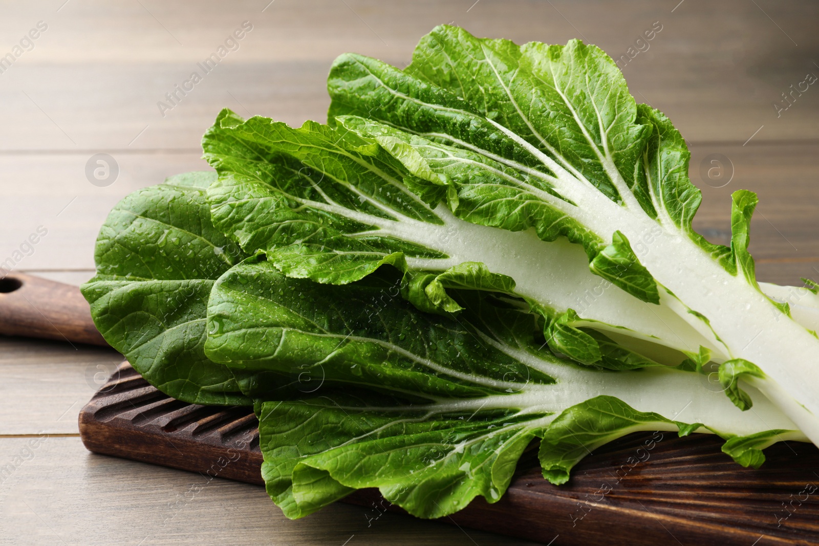 Photo of Leaves of fresh green pak choy cabbage with water drops on wooden table, closeup