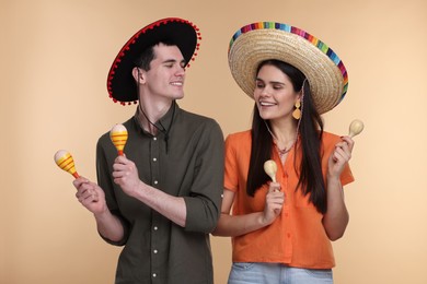 Lovely couple woman in Mexican sombrero hats with maracas on beige background