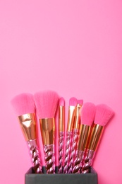 Organizer with set of makeup brushes on pink background, top view. Space for text