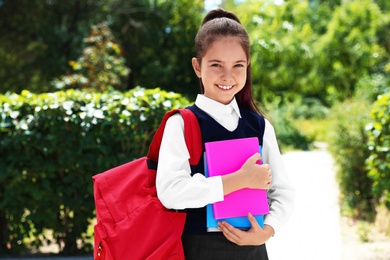 Cute little girl in school uniform with backpack and stationery on street