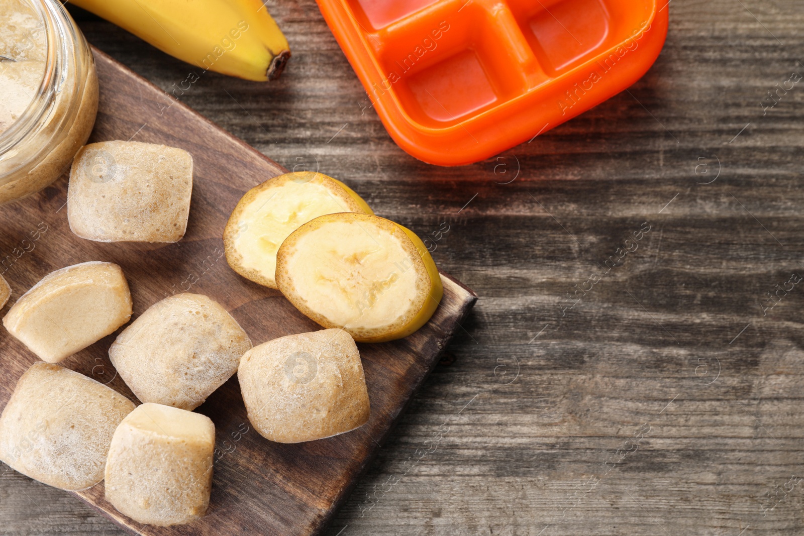 Photo of Frozen banana puree cubes and ingredient on wooden table, flat lay. Space for text