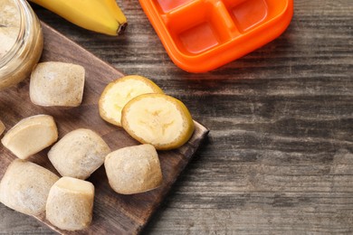 Photo of Frozen banana puree cubes and ingredient on wooden table, flat lay. Space for text