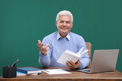 Photo of Portrait of senior teacher with laptop at table against green chalkboard