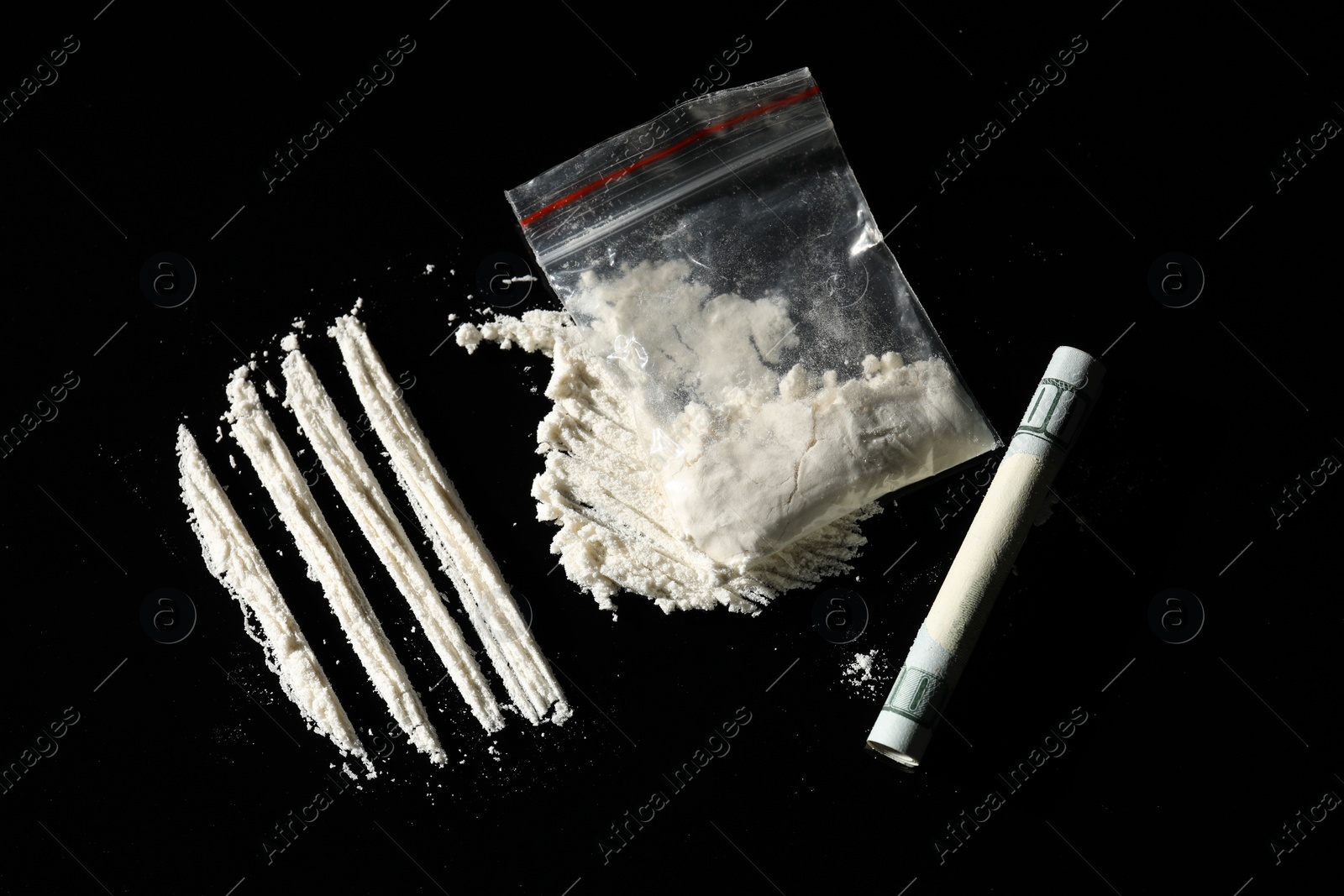 Photo of Drug addiction. Plastic bag with cocaine and rolled dollar banknote on black background, flat lay