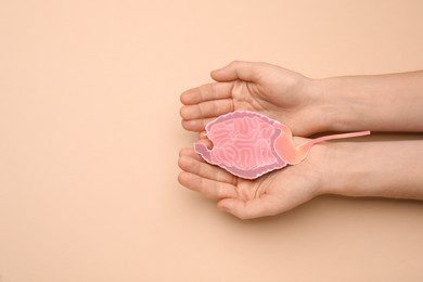 Woman holding paper cutout of small intestine on beige background, top view. Space for text