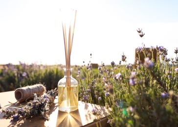 Photo of Reed air freshener on wooden table in blooming lavender field