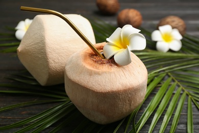 Photo of Fresh coconut with drinking straw and flower on black wooden table, closeup