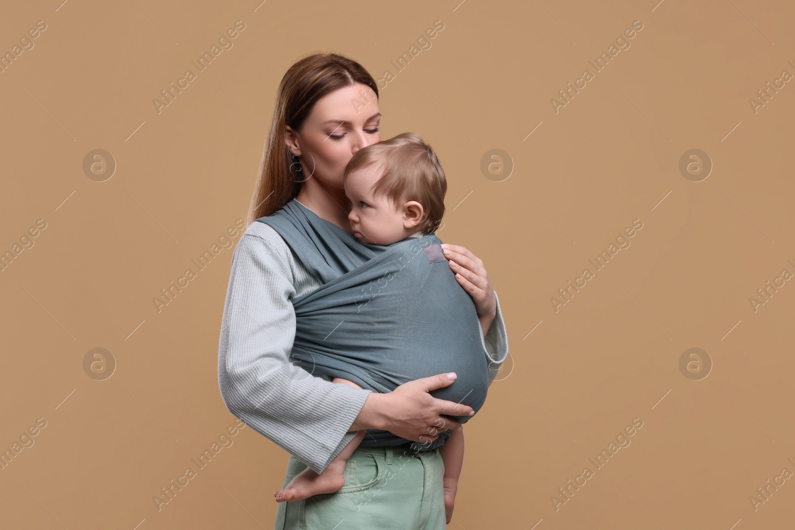 Photo of Mother holding her child in baby wrap on light brown background