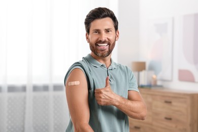 Photo of Man with sticking plaster on arm after vaccination showing thumbs up at home