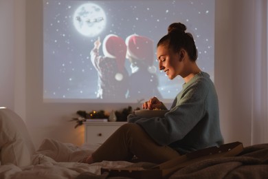 Woman with popcorn watching Christmas movie via video projector at home