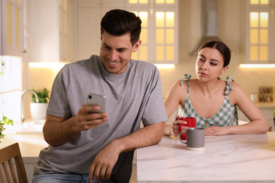 Distrustful woman peering into boyfriend's smartphone at home. Jealousy in relationship