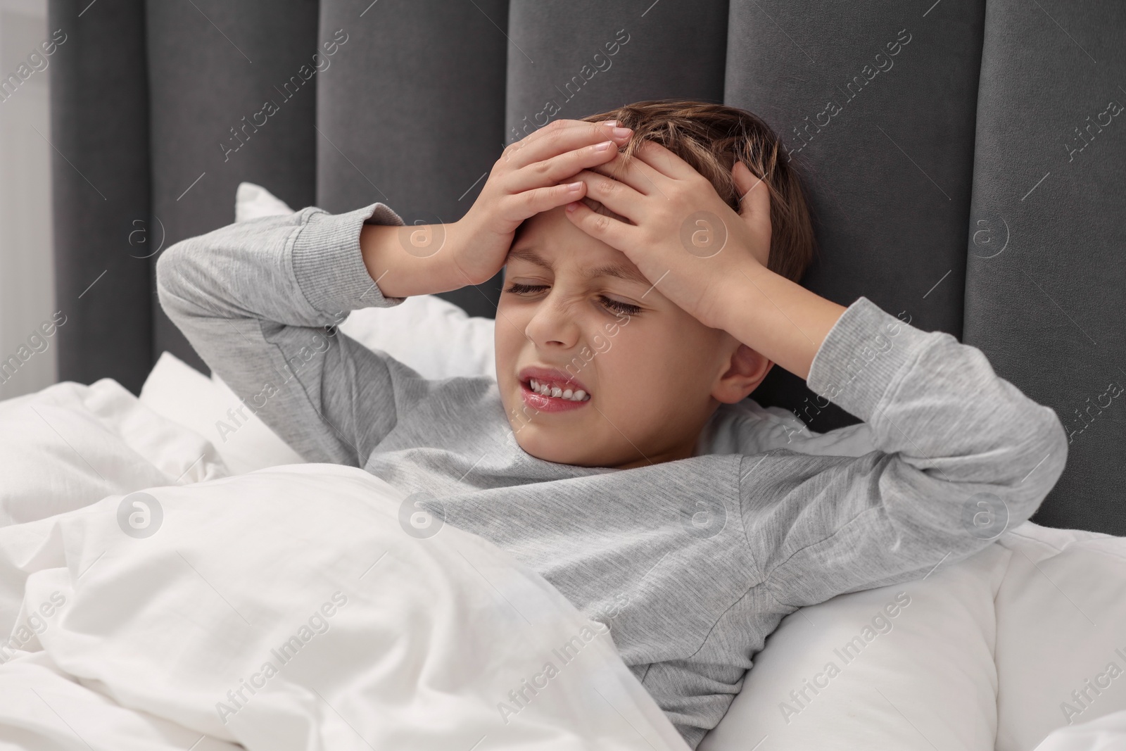 Photo of Little boy suffering from headache in bed at home