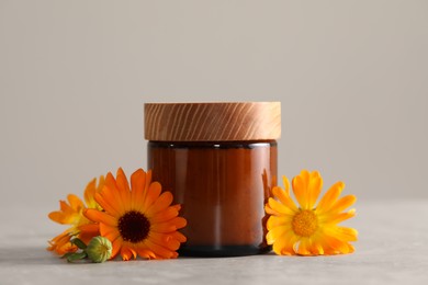Jar of cosmetic product and beautiful calendula flowers on light grey table, closeup