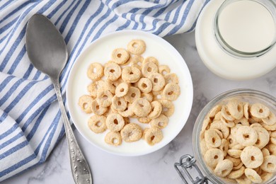 Photo of Breakfast cereal. Tasty corn rings, milk and spoon on white marble table, flat lay