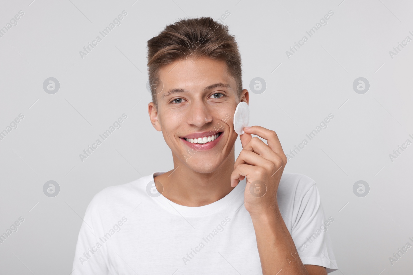 Photo of Handsome man cleaning face with cotton pad on light background