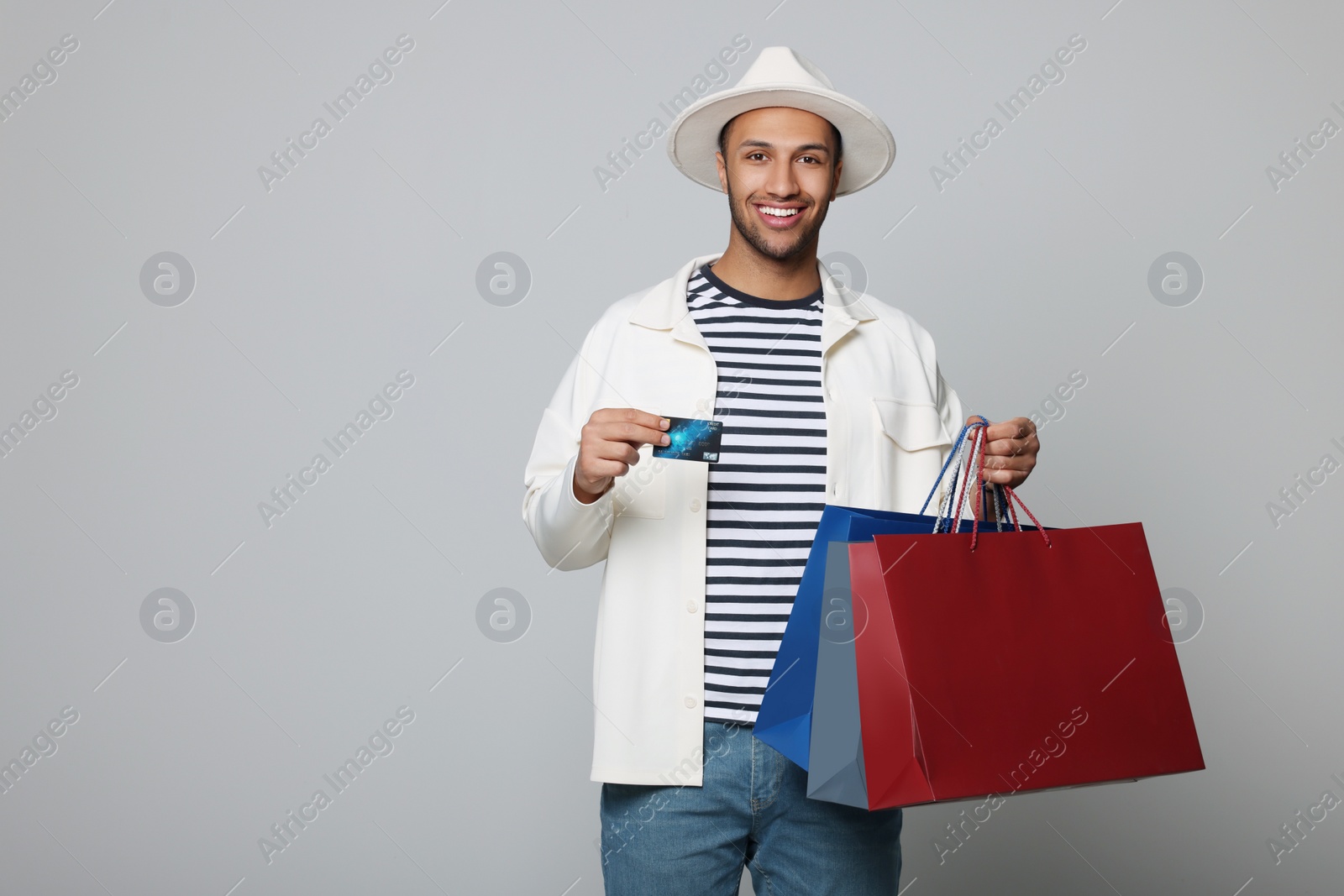 Photo of Happy African American man in hat with shopping bags and credit card on light grey background. Space for text