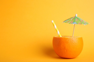 Orange with straw and small paper umbrella as summer cocktail on yellow background. Space for text