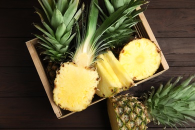 Photo of Tasty cut pineapples in crate on wooden table, flat lay