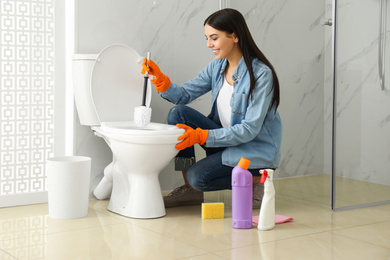 Young woman cleaning toilet bowl in bathroom