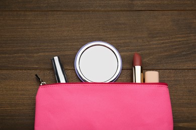 Photo of Stylish pocket mirror and cosmetic bag with makeup products on wooden table, flat lay