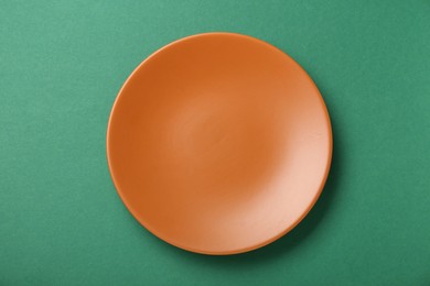 Photo of Empty orange ceramic plate on green background, top view