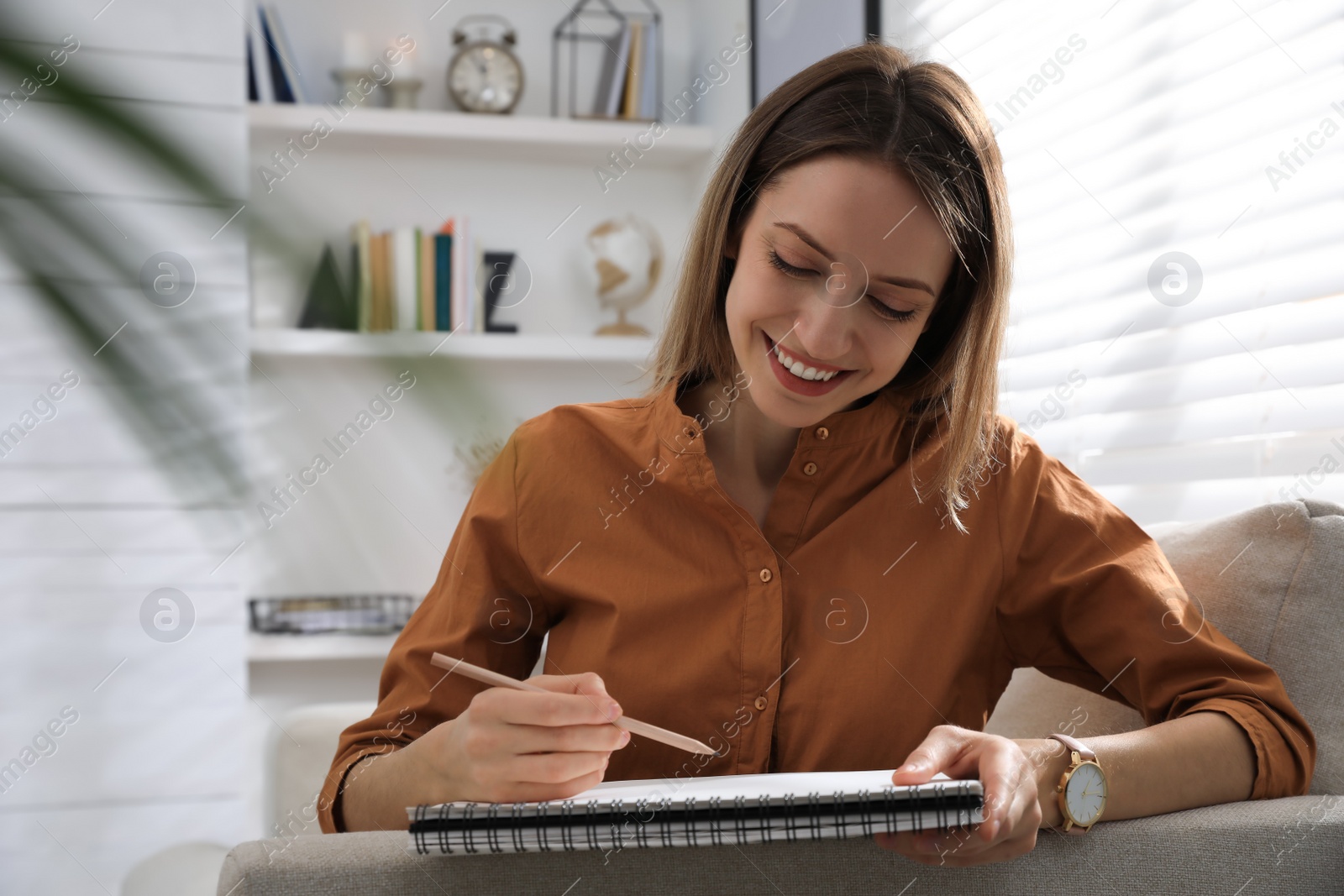 Photo of Young woman drawing in sketchbook with pencil at home