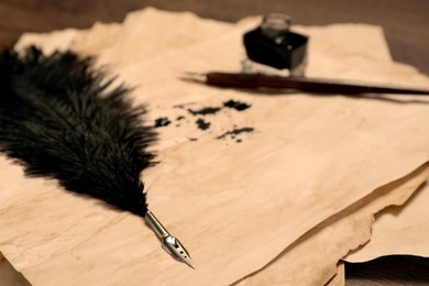 Different pens, inkwell and vintage parchment with ink stains on table, closeup