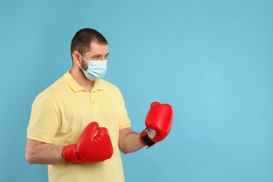 Photo of Man with protective mask and boxing gloves on light blue background, space for text. Strong immunity concept