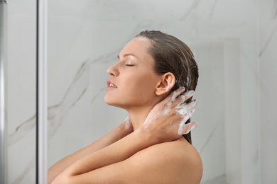 Beautiful young woman washing hair in shower at home