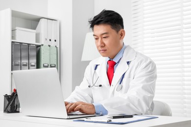 Photo of Doctor with laptop consulting patient at white desk in clinic. Online medicine