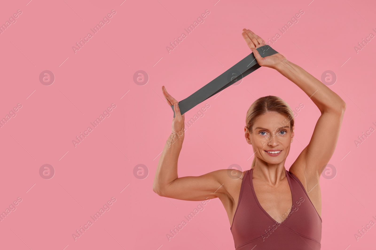 Photo of Woman exercising with elastic resistance band on pink background. Space for text