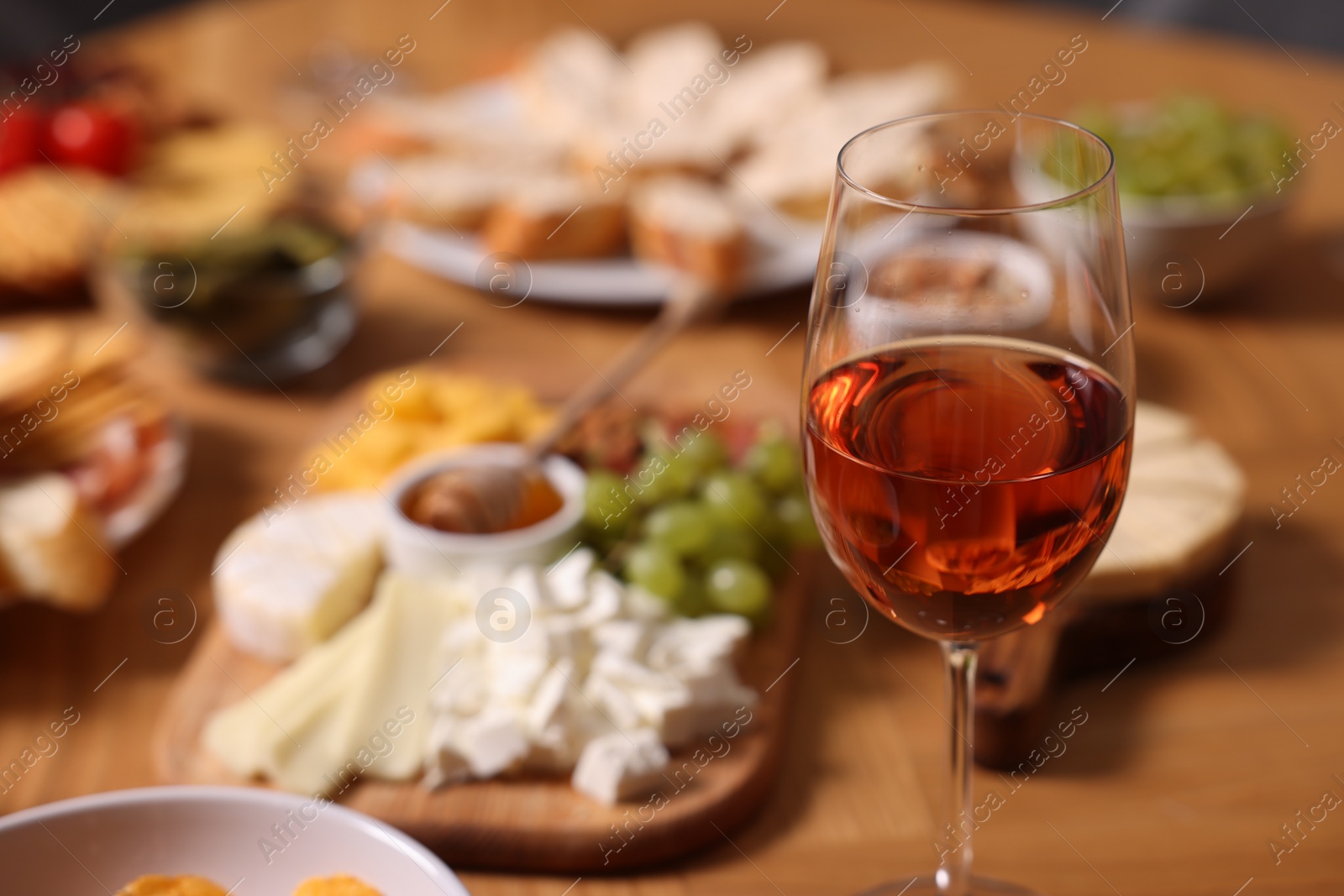 Photo of Glass of rose wine and appetizers served on wooden table, selective focus. Space for text