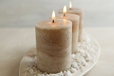 Plate with three burning candles and rocks on table