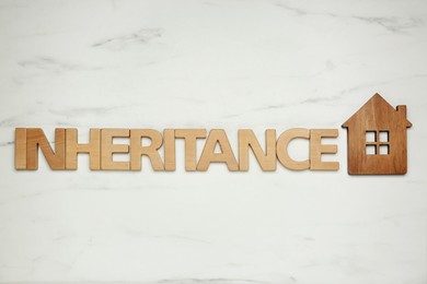 Photo of Word Inheritance made with wooden letters and house model on white marble background, flat lay